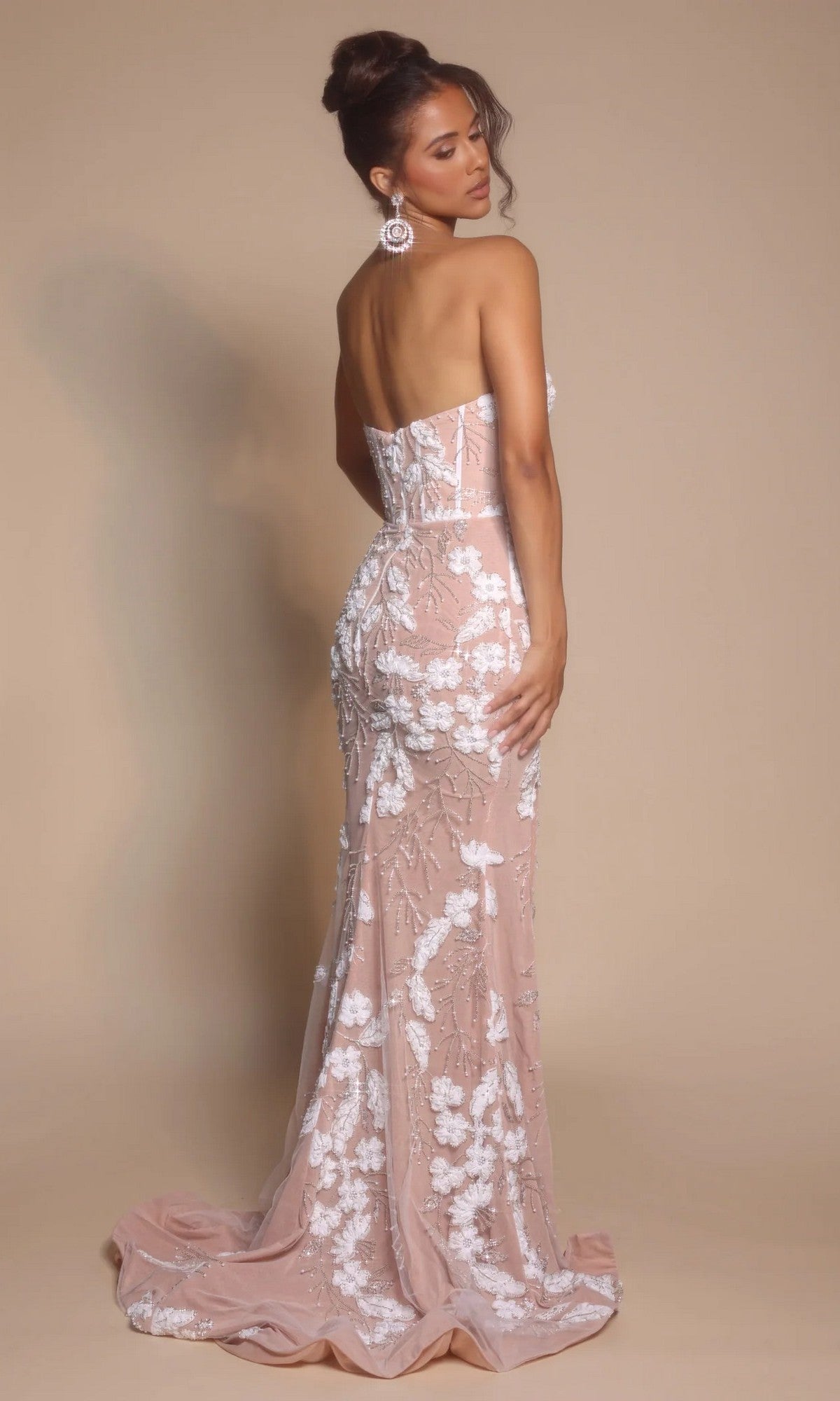 Woman in the Portia and Scarlett PS26074 long formal dress—strapless, sweetheart neckline, floor-length pink gown with white floral embroidery—stands facing away, head turned to the side against a neutral background.